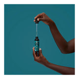 Hand holding a dropper over a bottle labeled 'Nubian Heritage' against a teal background